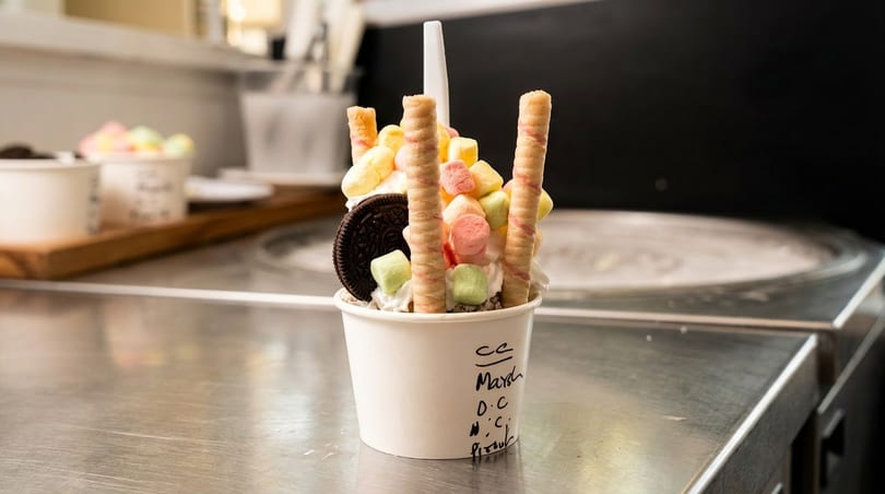 Rolled ice cream with colorful marshmallows, wafer sticks, and an Oreo cookie in a cup.