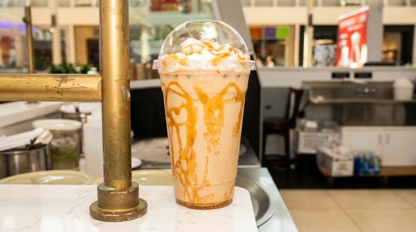 A caramel iced coffee with whipped cream and caramel drizzle sits on a white counter.